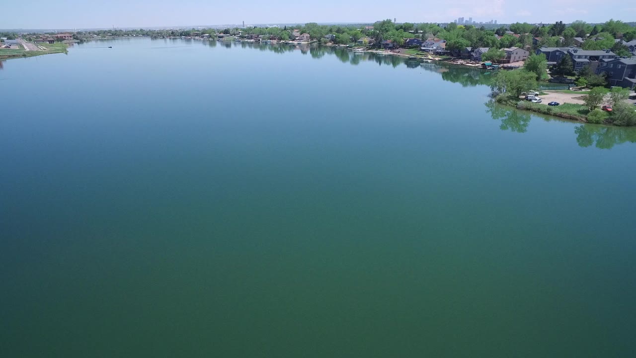 Aerial view over blue-green lake water toward a residential shoreline.