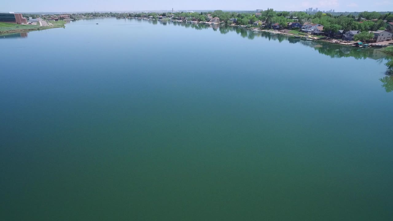 Wide aerial view over blue-green water toward a tree-lined shore.