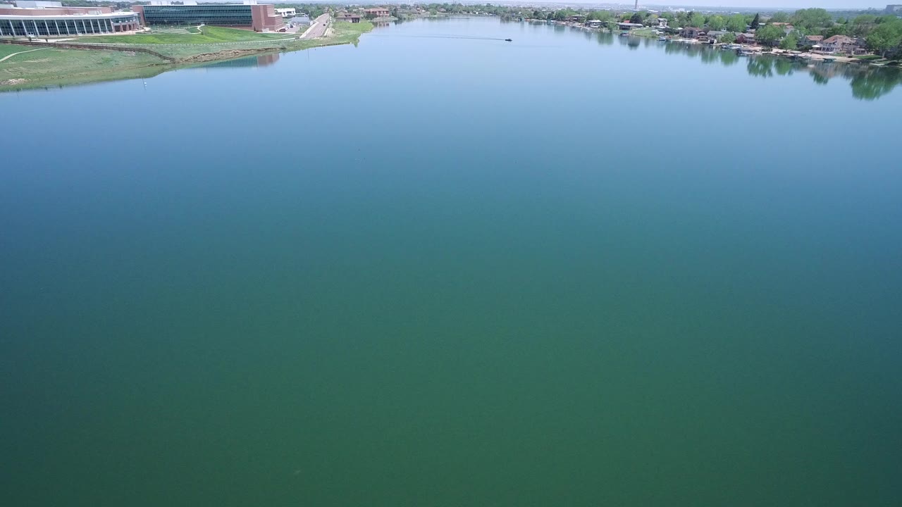 Wide blue-green water with grassy banks and distant buildings.