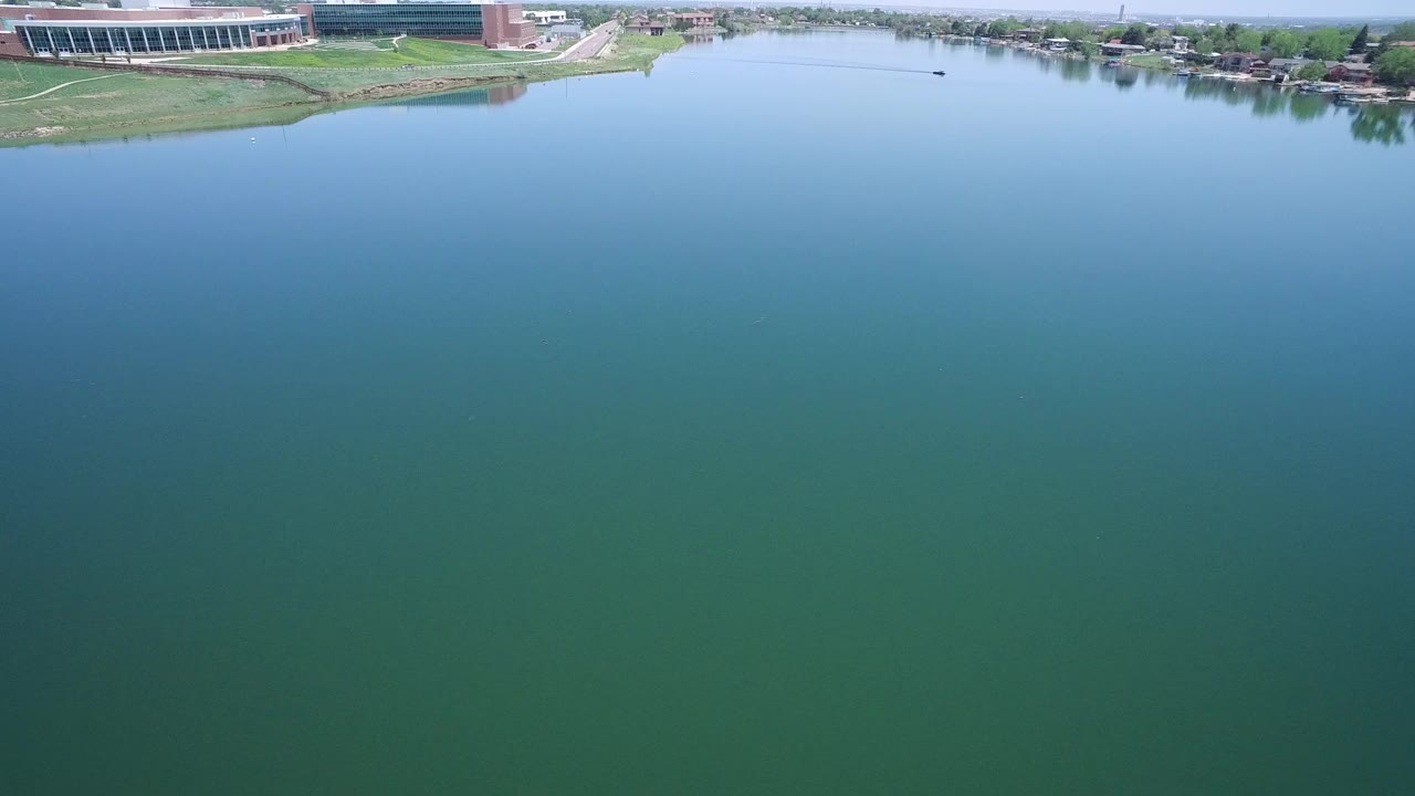 Aerial view over greenish lake water with shoreline and building at top.