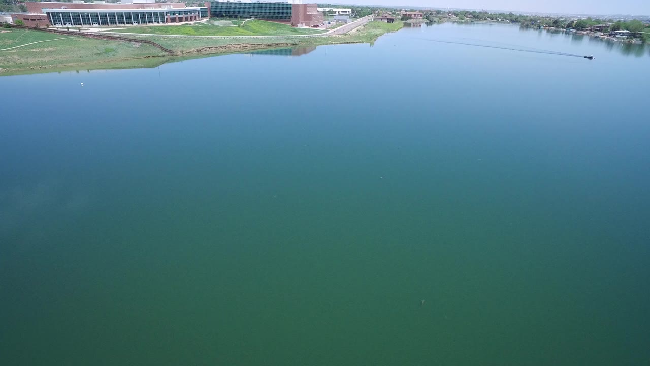 Aerial view over blue-green water with a large building along the far shoreline.