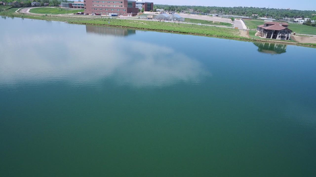 Aerial view of a lake reflecting clouds beside shoreline buildings.