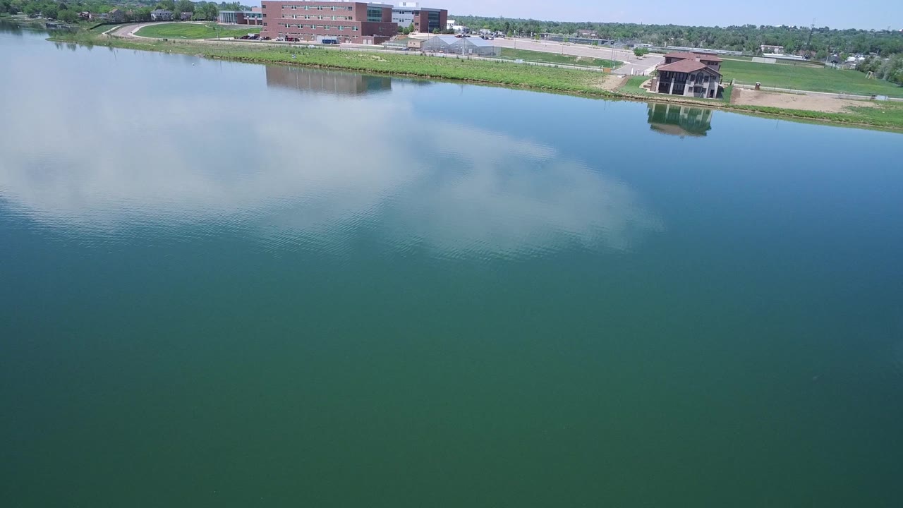 Calm lake water with cloud reflection and a pavilion along the far shoreline.