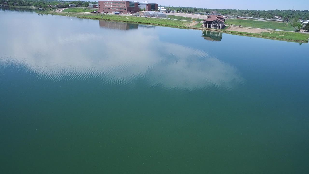 Wide aerial lake view with shoreline buildings and reflected sky.