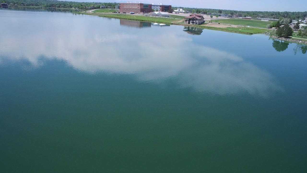 Aerial view over a lake with cloud reflections and a grassy shoreline.