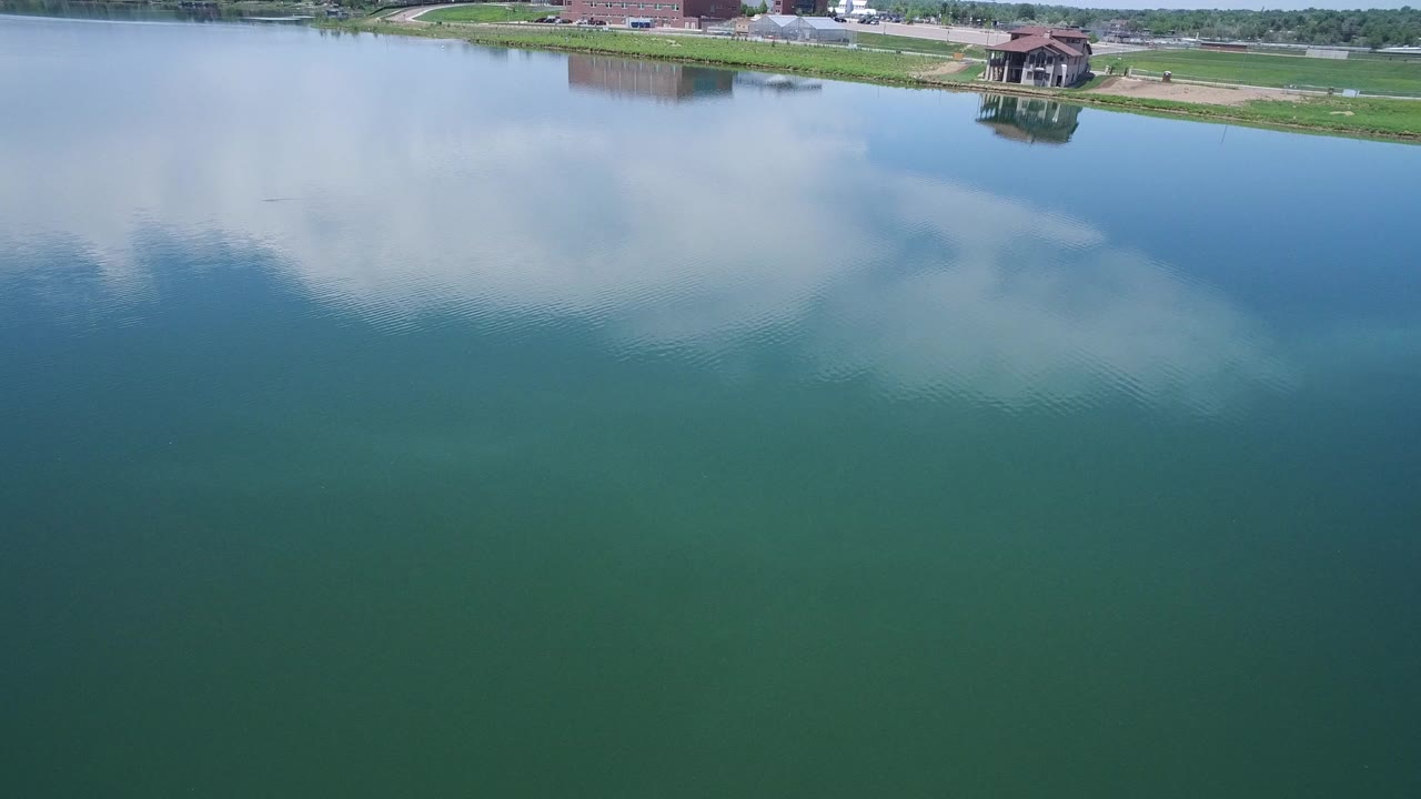 Blue green water with cloud reflection and grassy shoreline at the top.