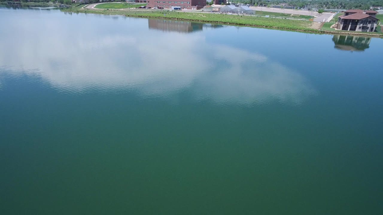 The water fills most of the frame in Westminster, Colorado, with pale cloud reflection, slight ripples, a thin green bank, and no visible people.