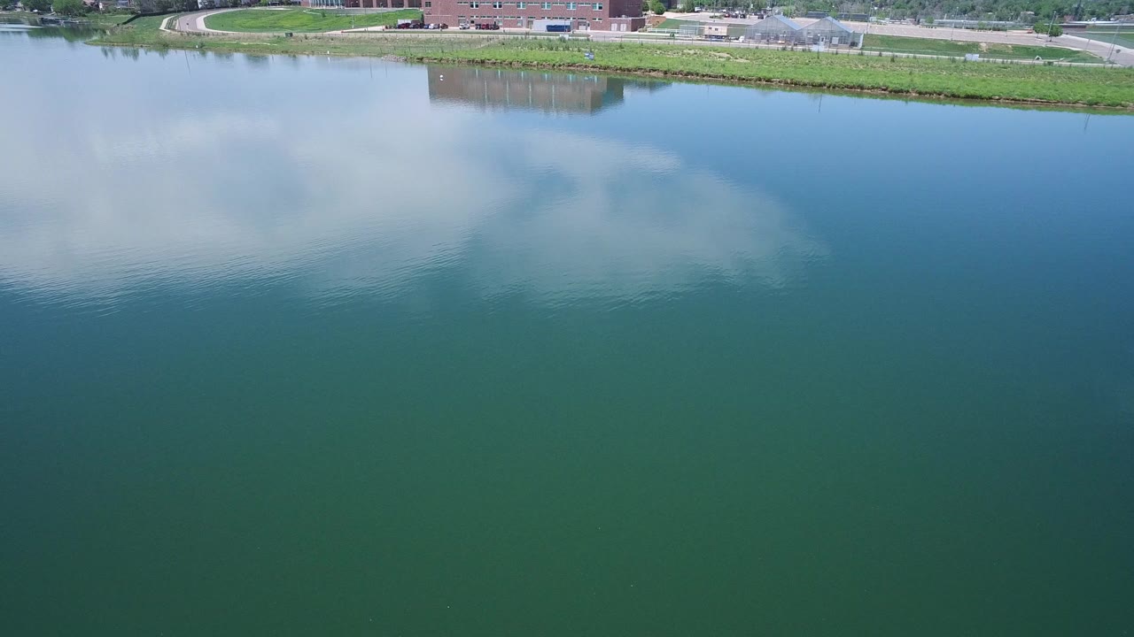 Blue-green lake water with cloud reflections and a narrow grassy shoreline.