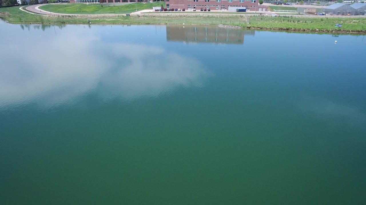 Aerial view of green-blue water with cloud reflections and a narrow shoreline.