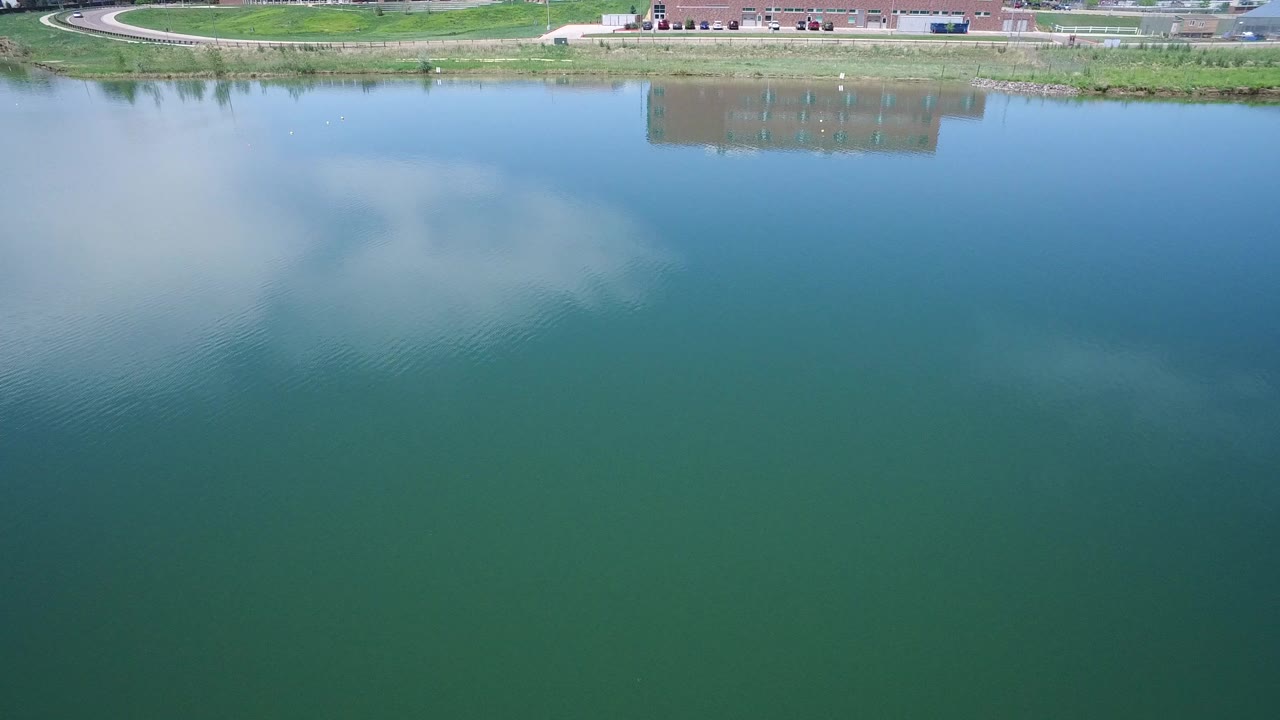 Aerial view of blue-green lake water and distant grassy shoreline.