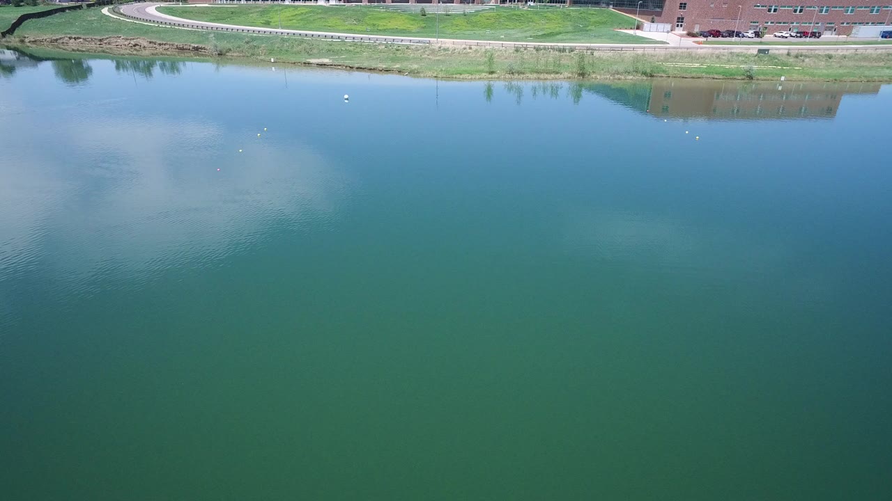 Blue-green water reflecting clouds with grassy shoreline and trail at the top.