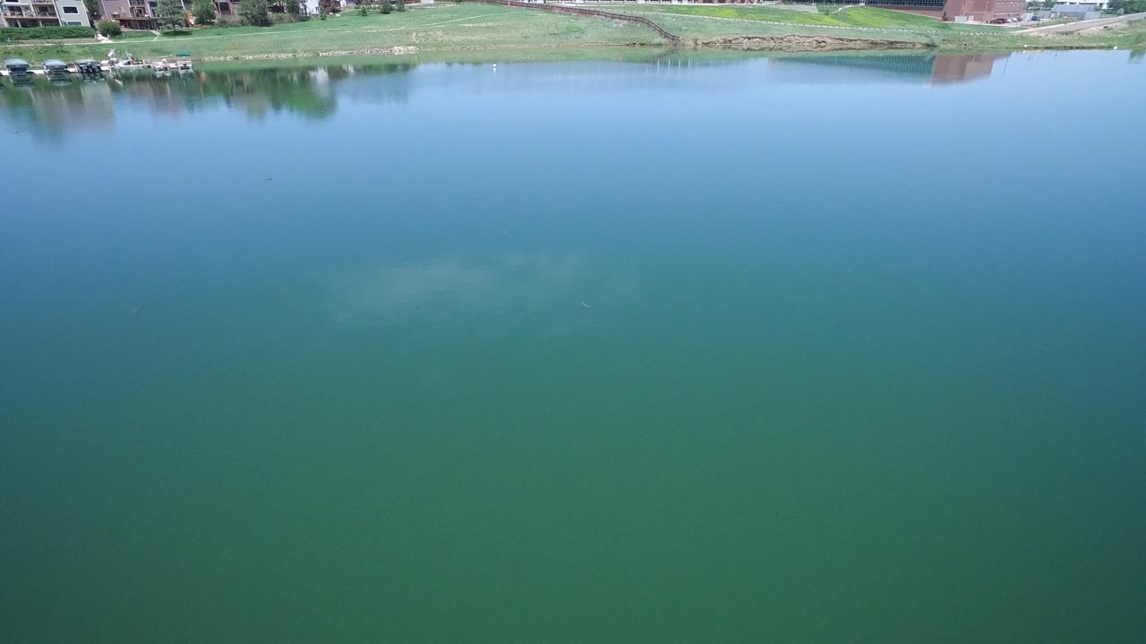 Aerial view over a green lake with houses along the far shore