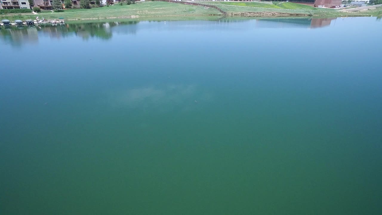 Aerial view of the green-blue Westminster lake with the shoreline and homes compressed near the top of the frame and no visible people.