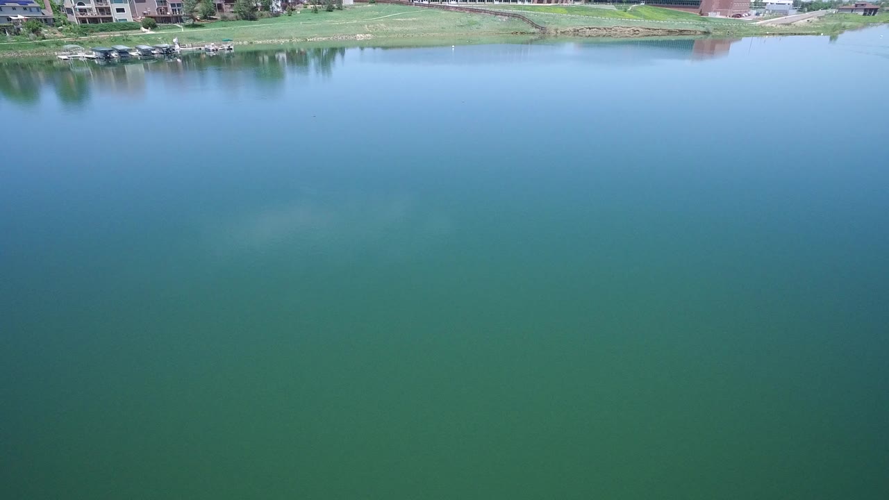 Aerial view of blue-green lake water with homes and shoreline at the top.