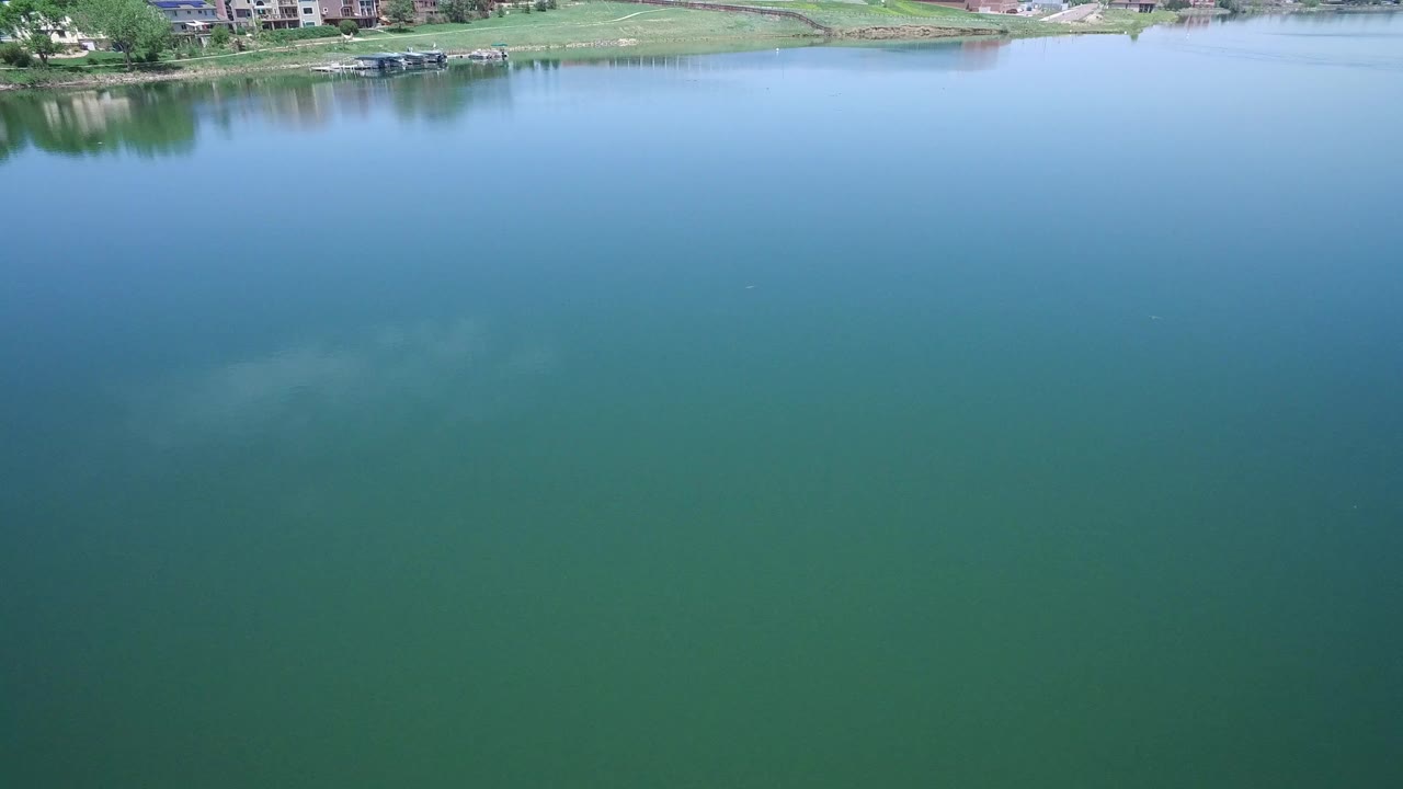The lake surface fills the Westminster, Colorado aerial frame, with soft cloud reflection in the water and a narrow strip of far shoreline with homes near the upper edge, no visible people.