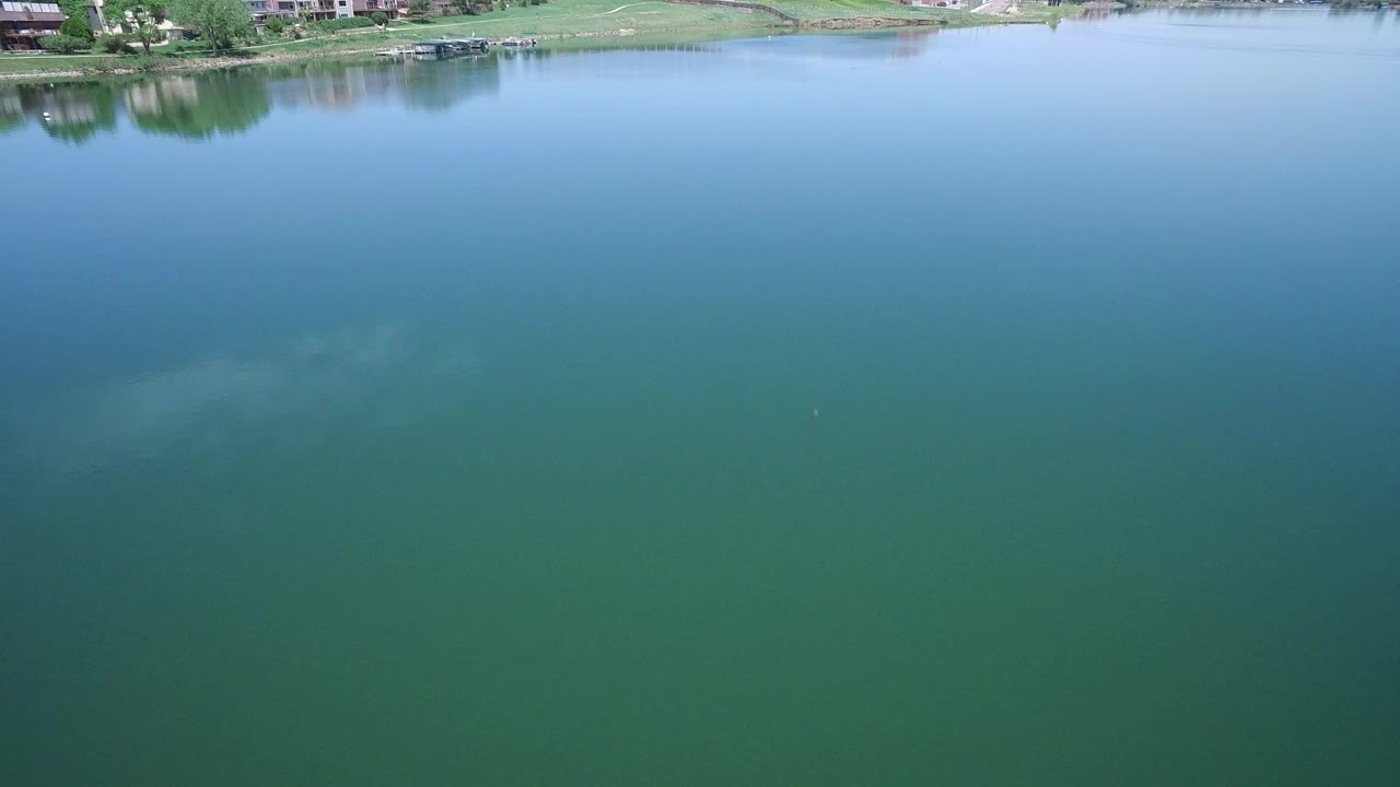 Second frame shows calm blue and green lake water in Westminster, Colorado, with the far bank and small residential structures near the top, no visible people.
