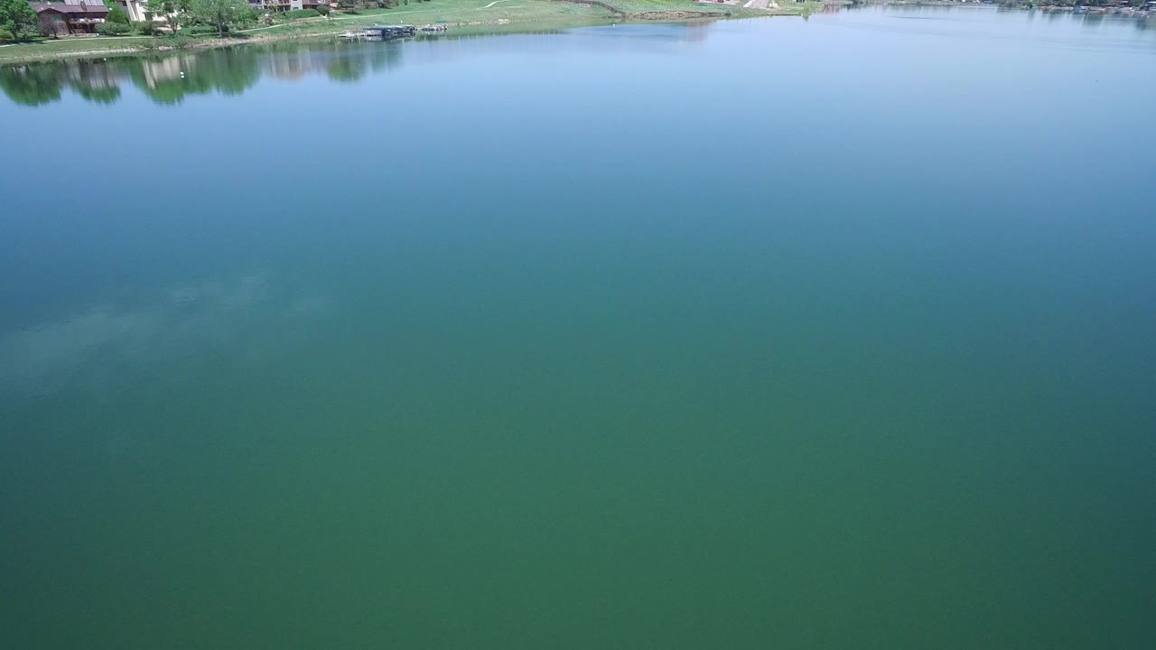 Blue-green lake water with grassy shore and homes at the top edge.