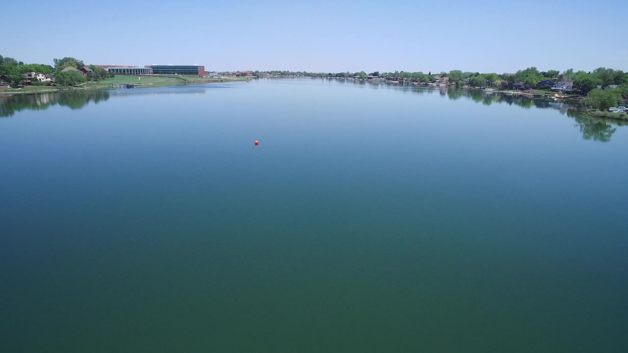 Wide lake with distant houses, trees, and pale blue sky