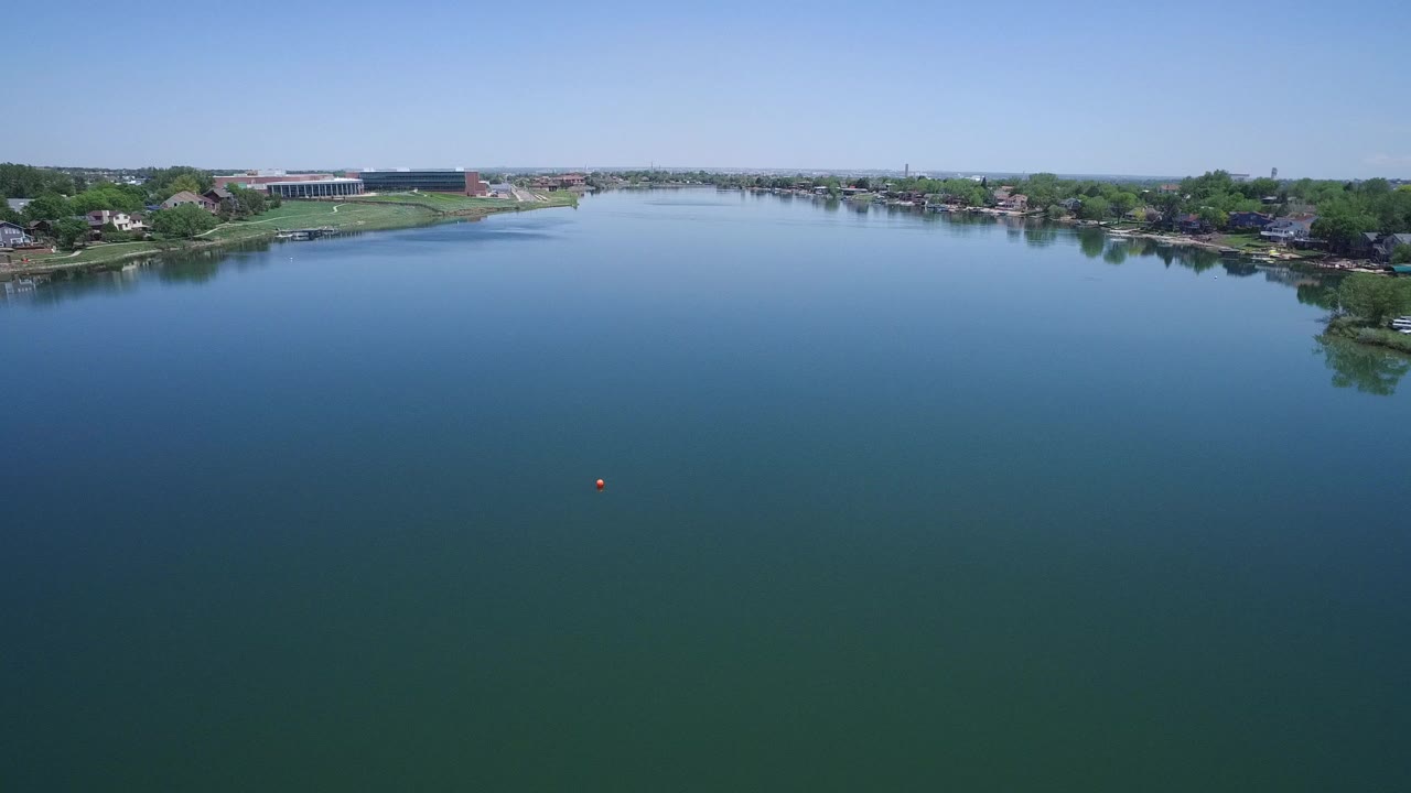 Wide aerial view over blue-green water with suburban shoreline and clear sky.