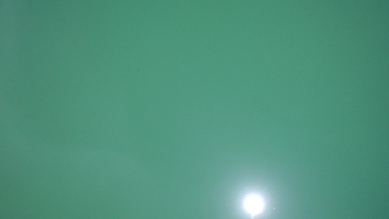 Top-down view of bright green water in Westminster, Colorado, with a white sun reflection near the lower portion and no visible people.