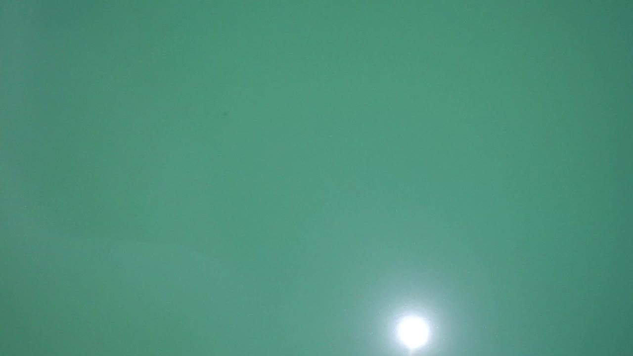 Overhead Westminster, Colorado water surface with a bright circular glare near the lower left and faint ripples across the green frame, with no visible people.