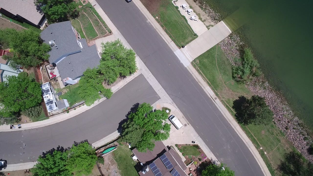Overhead view of suburban homes beside a road and pond edge.