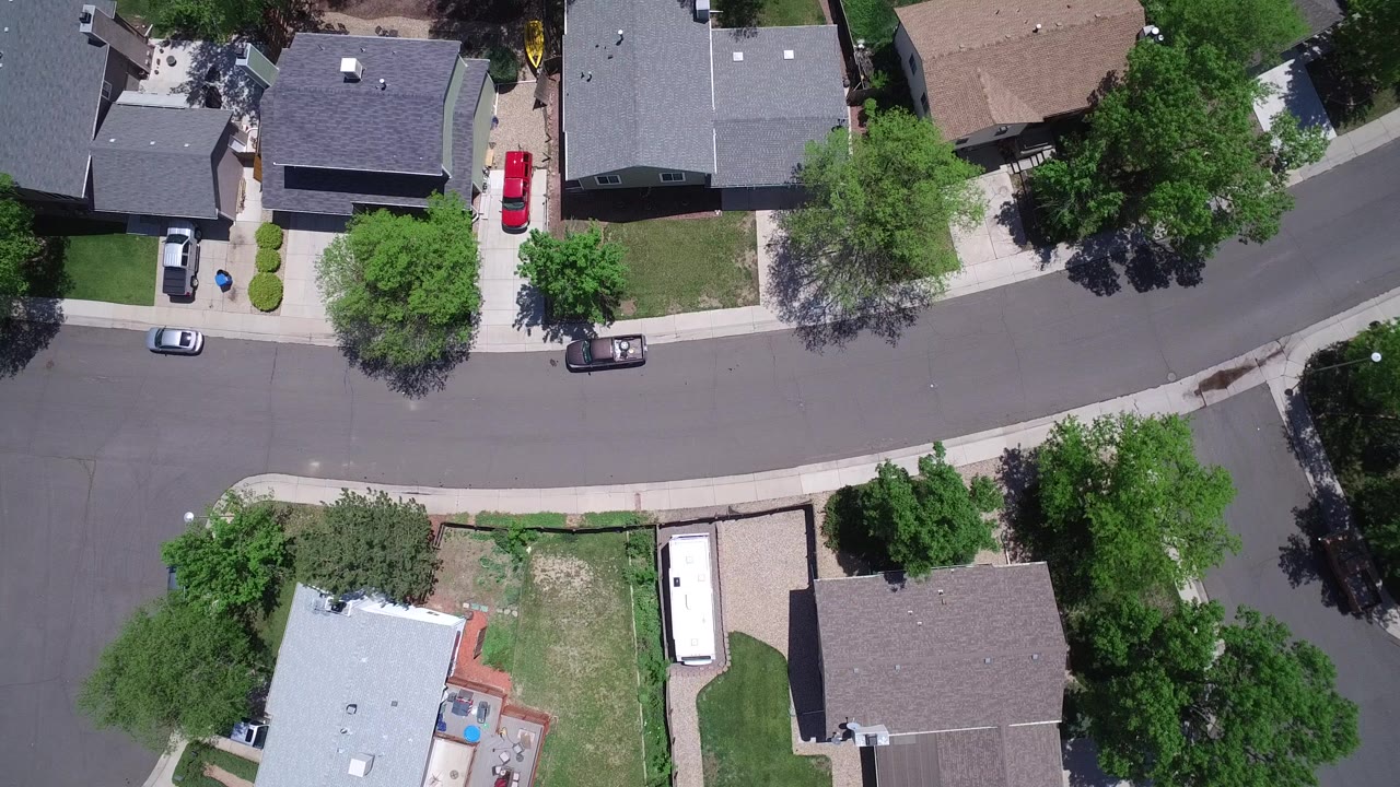Near-vertical aerial view over Westminster, Colorado homes, driveways, parked cars, lawns, trees, and a curved residential street, with no visible people.