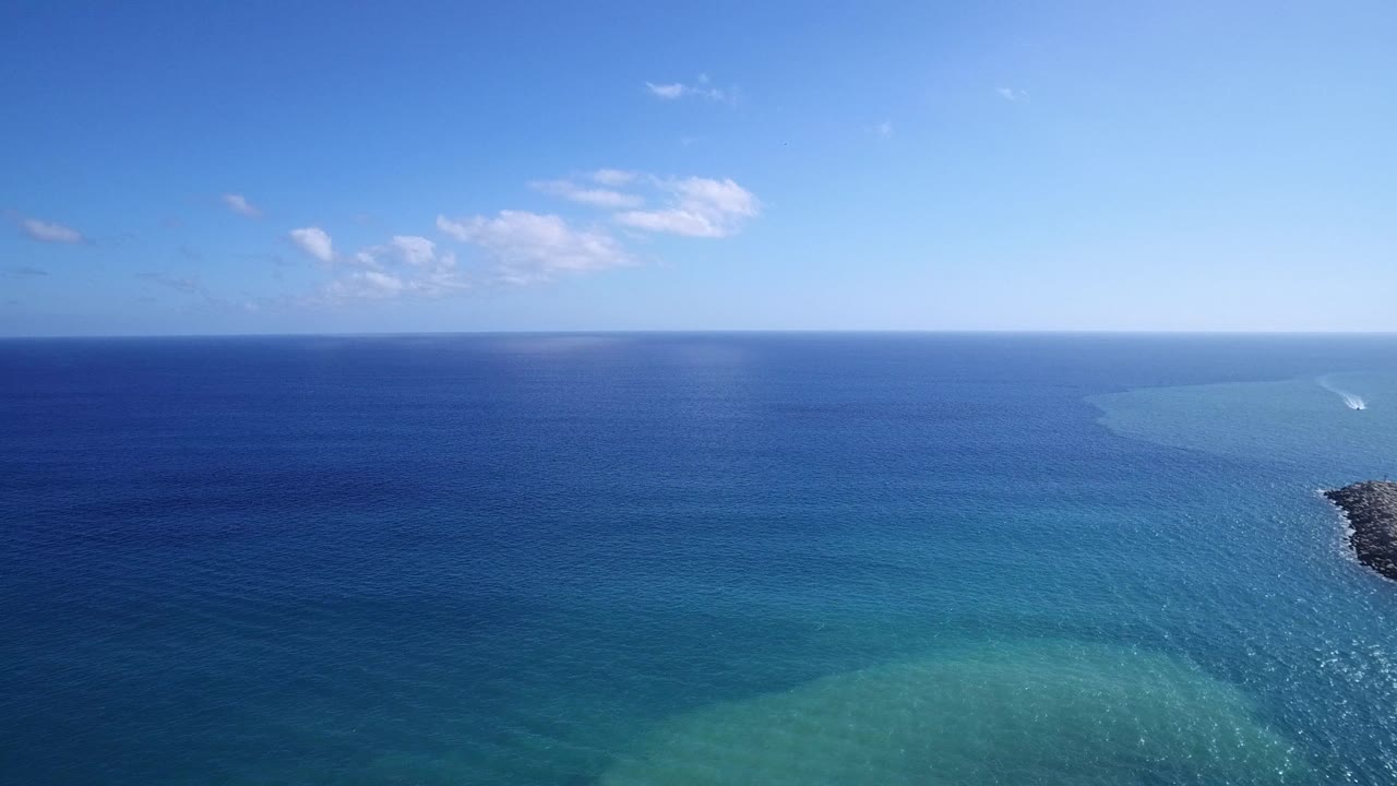 Blue sea, turquoise shallows, and a small rocky edge at right