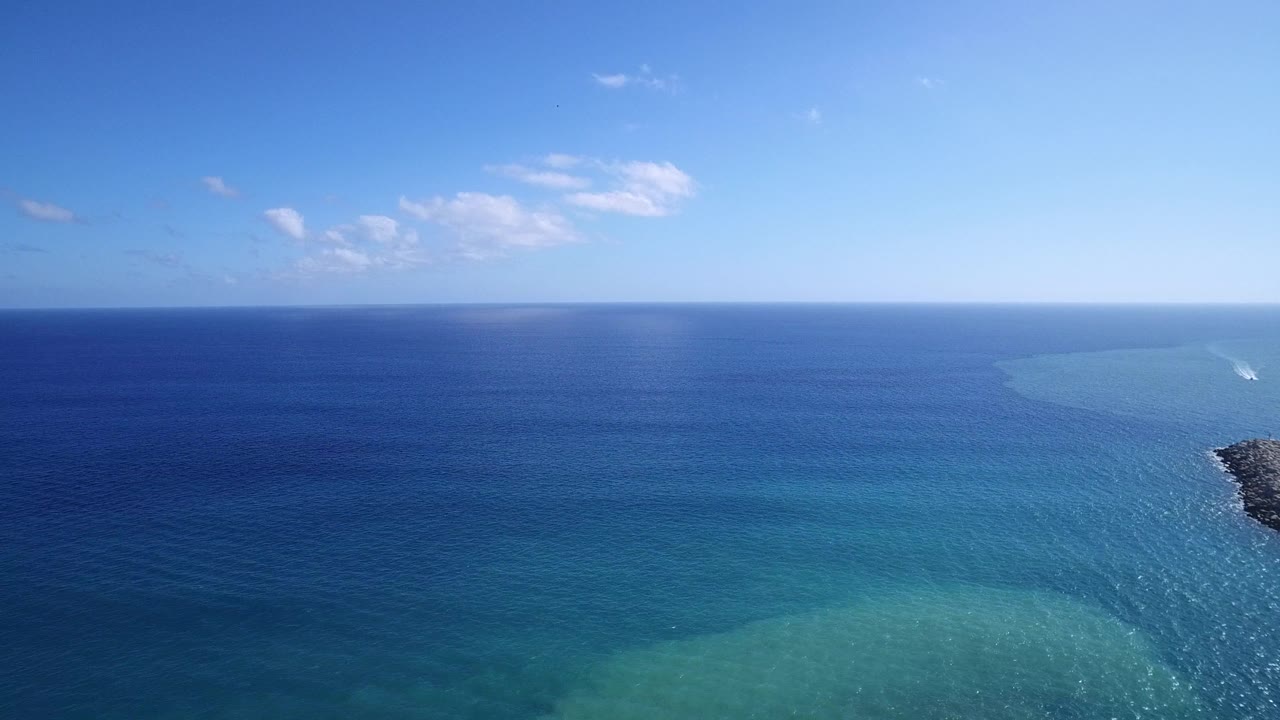 Blue sea and shallow coastal water under a clear sky with small clouds.