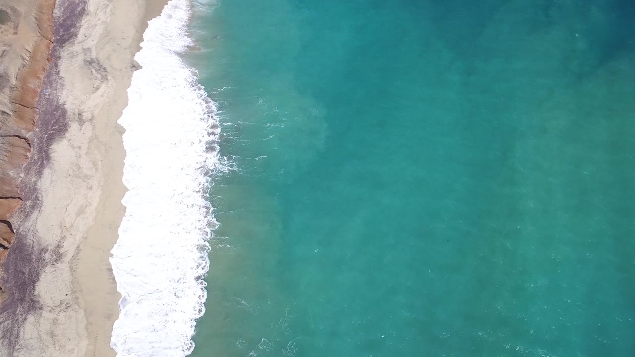 Surf washes onto a narrow sandy beach beside clear water.