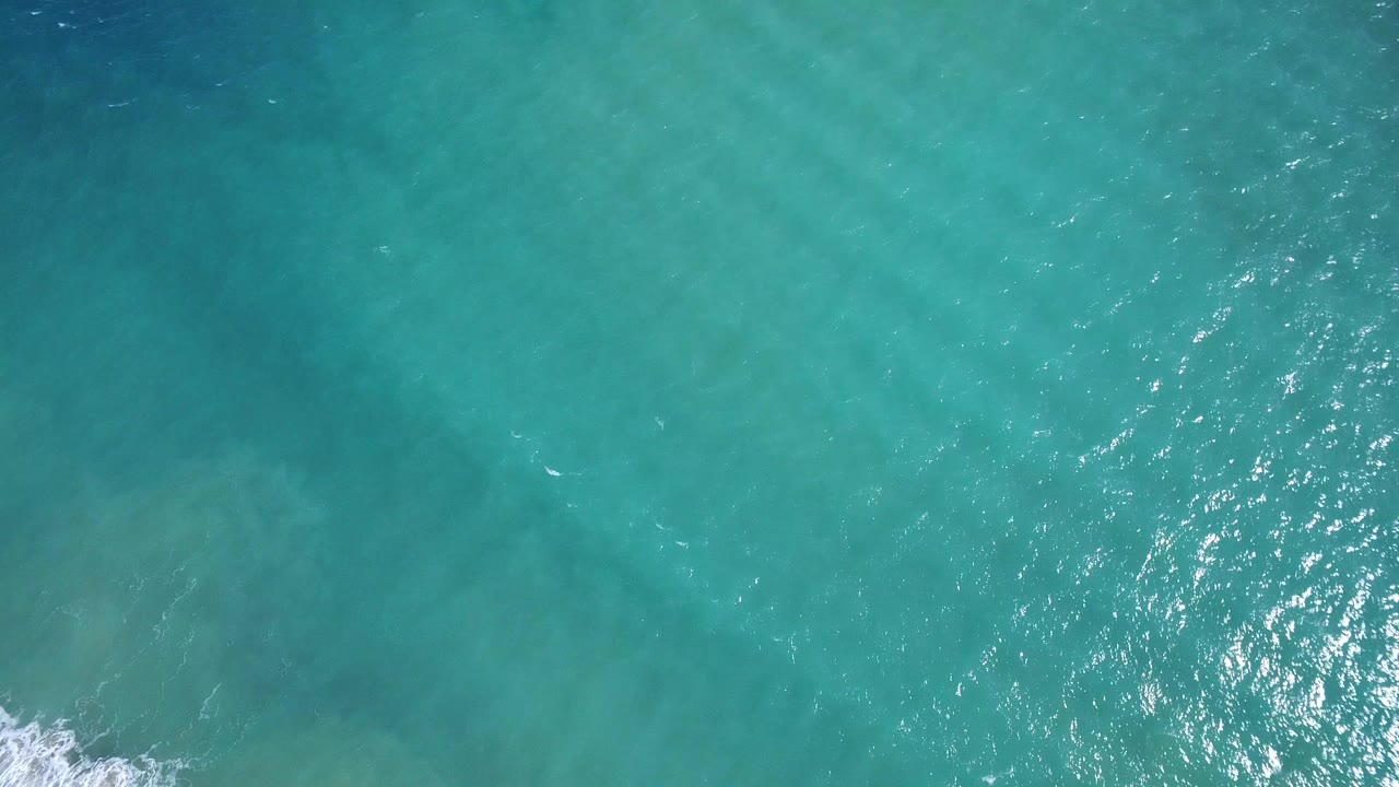 Overhead turquoise ocean water with small ripples and a bit of white surf at the lower left edge.