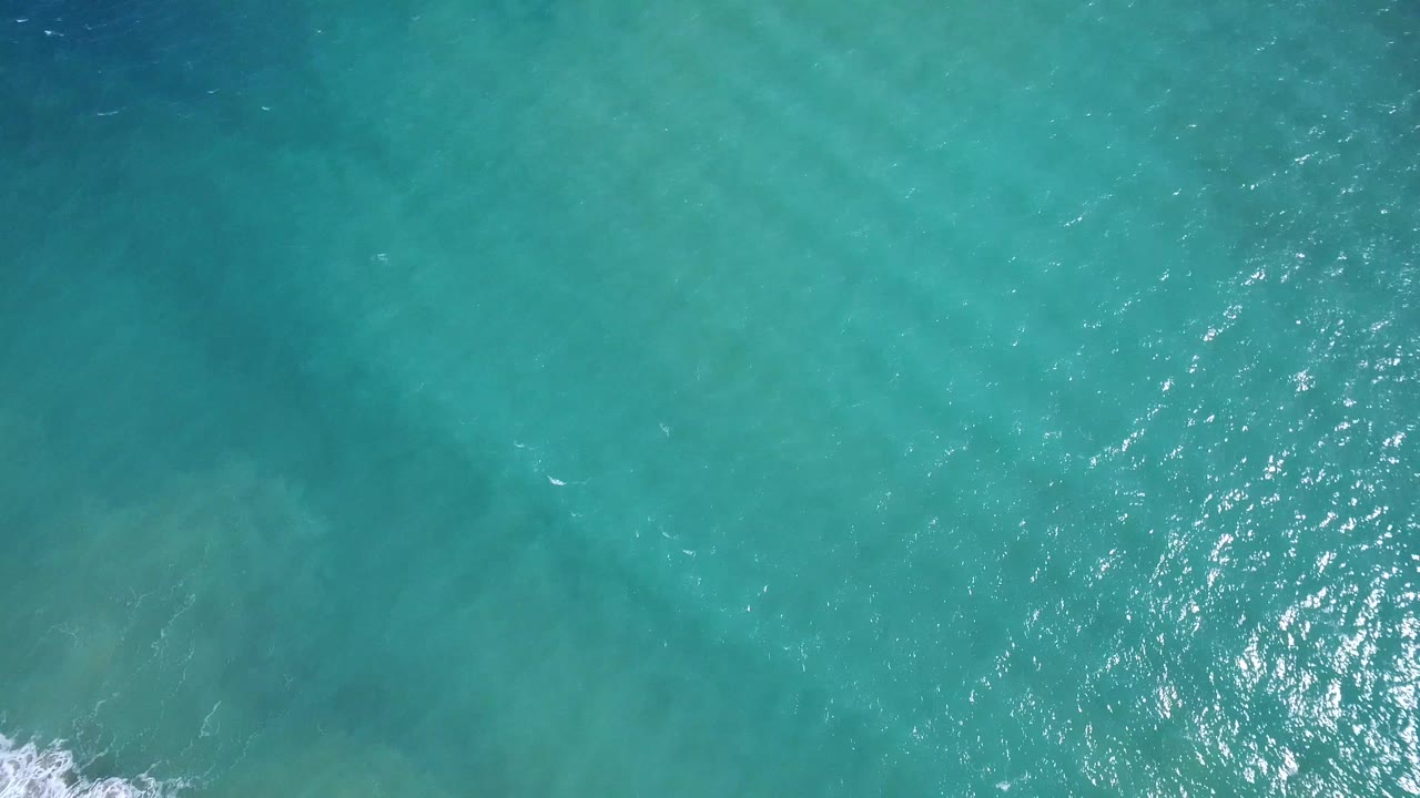 Overhead Playita ocean frame with turquoise water, a bright patch of sun reflection near the lower center, and no visible people.