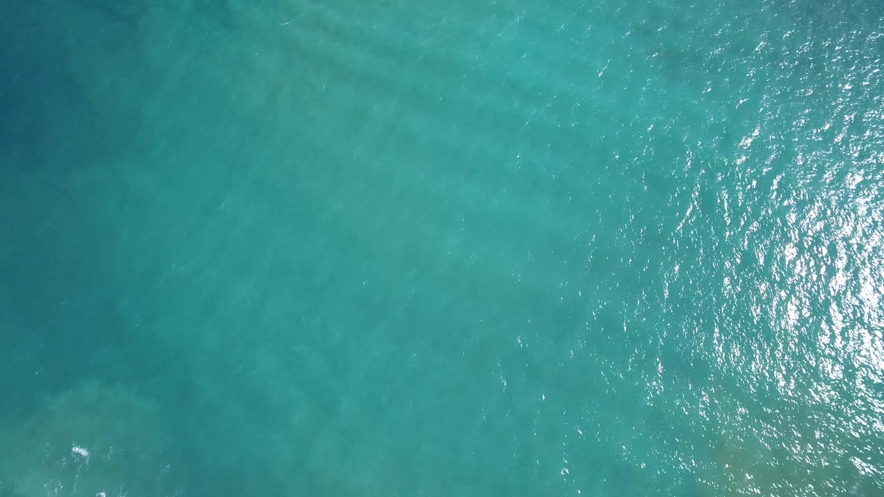 Turquoise ocean surface with bright reflection along the right edge.