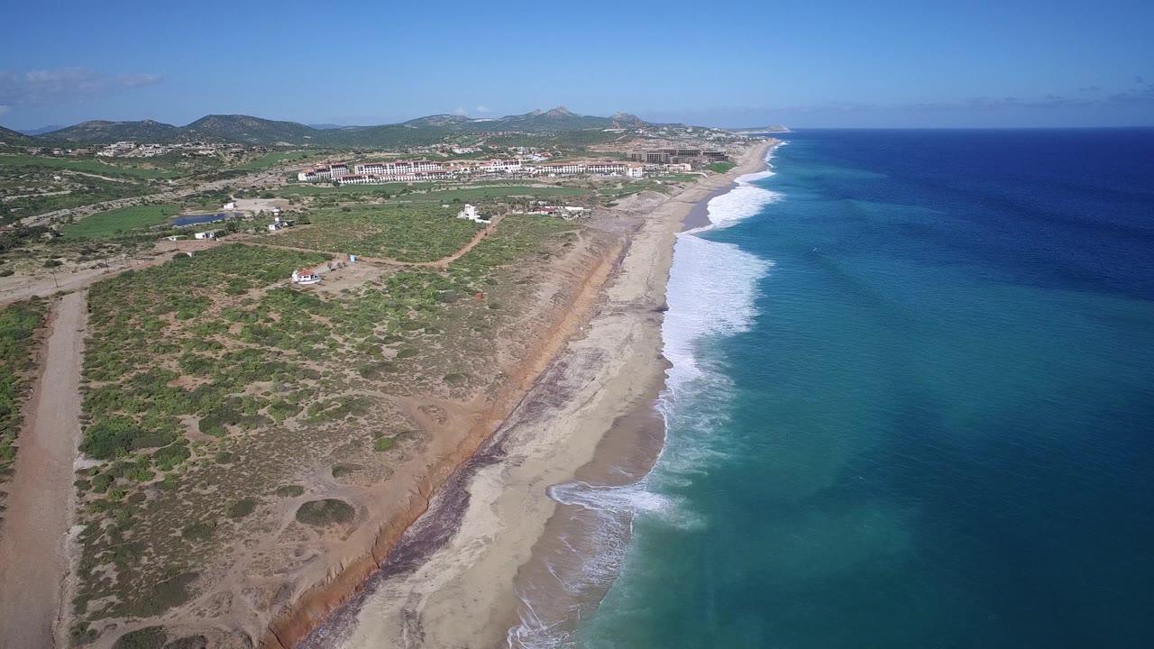 Wide aerial coastline with waves and town in the distance.