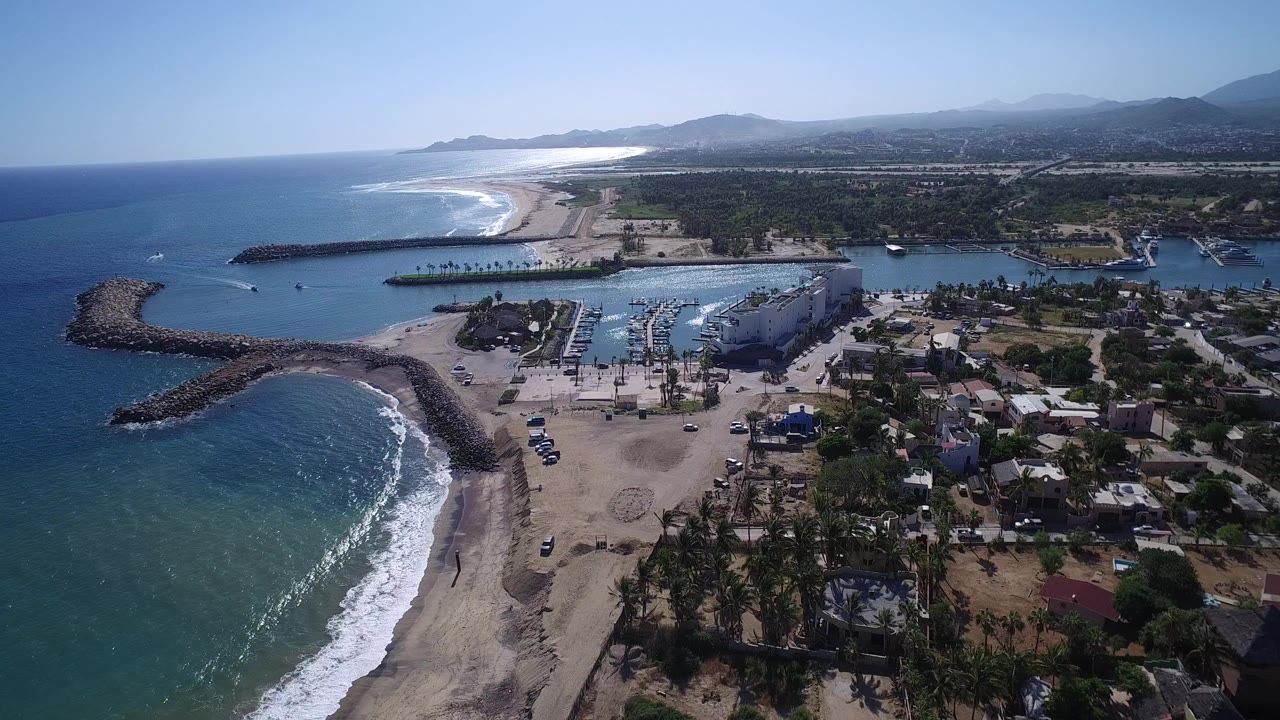 Aerial view of beach, rock breakwaters, marina, village, and blue sea.