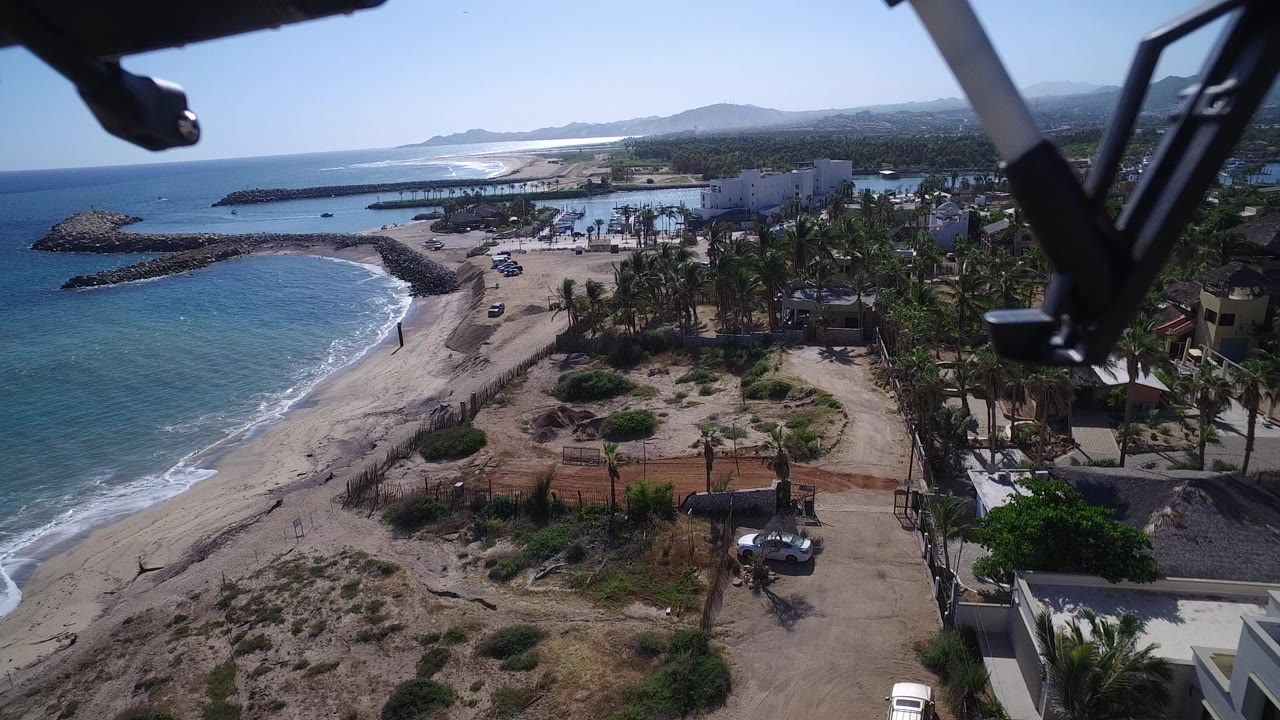 Aerial view of beach, blue ocean, palms, homes, and distant shoreline.