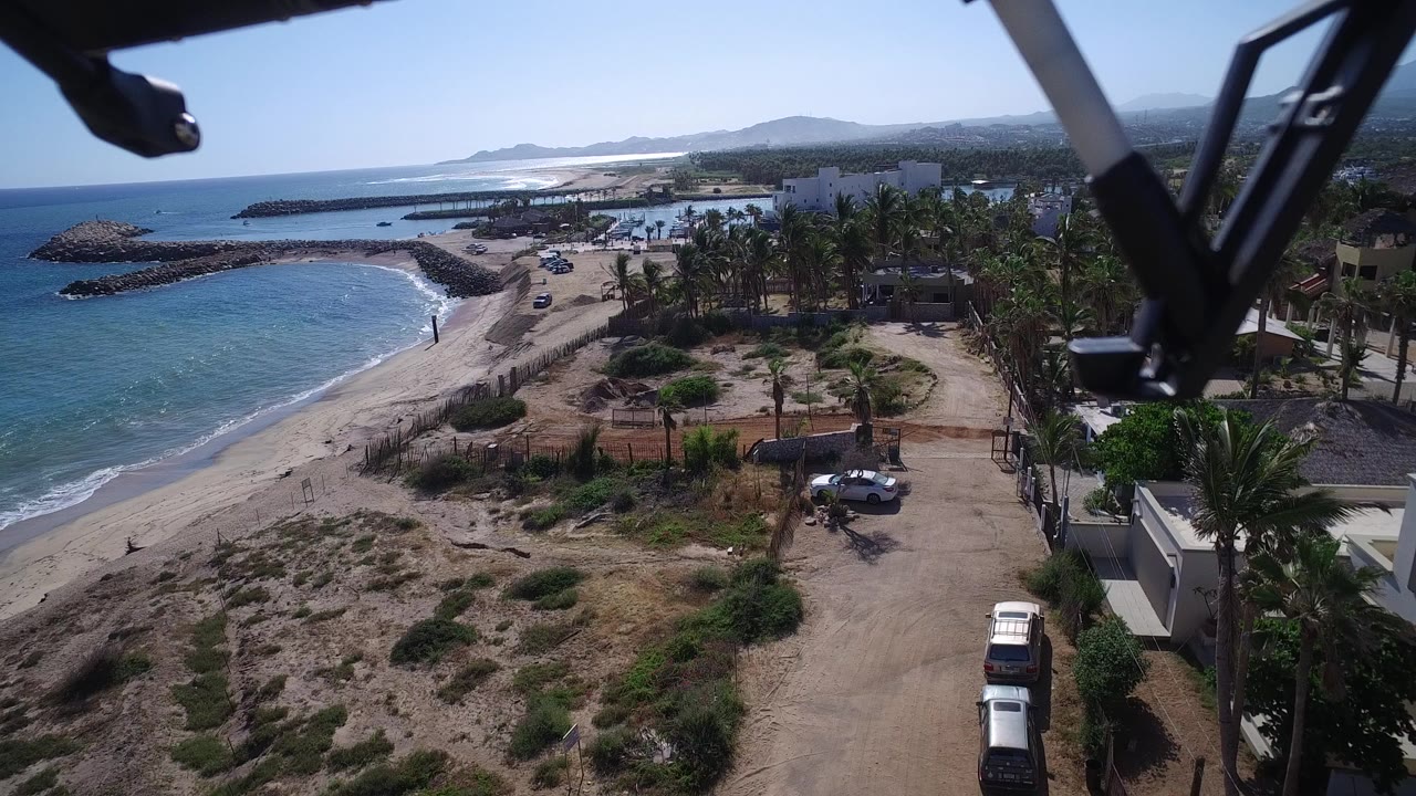 Aerial view of beach, blue water, dirt road, palms, and parked vehicles.