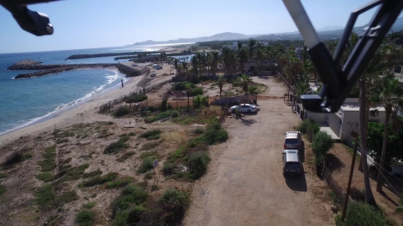 Elevated view over a sandy coastal road, beach, ocean, cars, and aircraft struts.