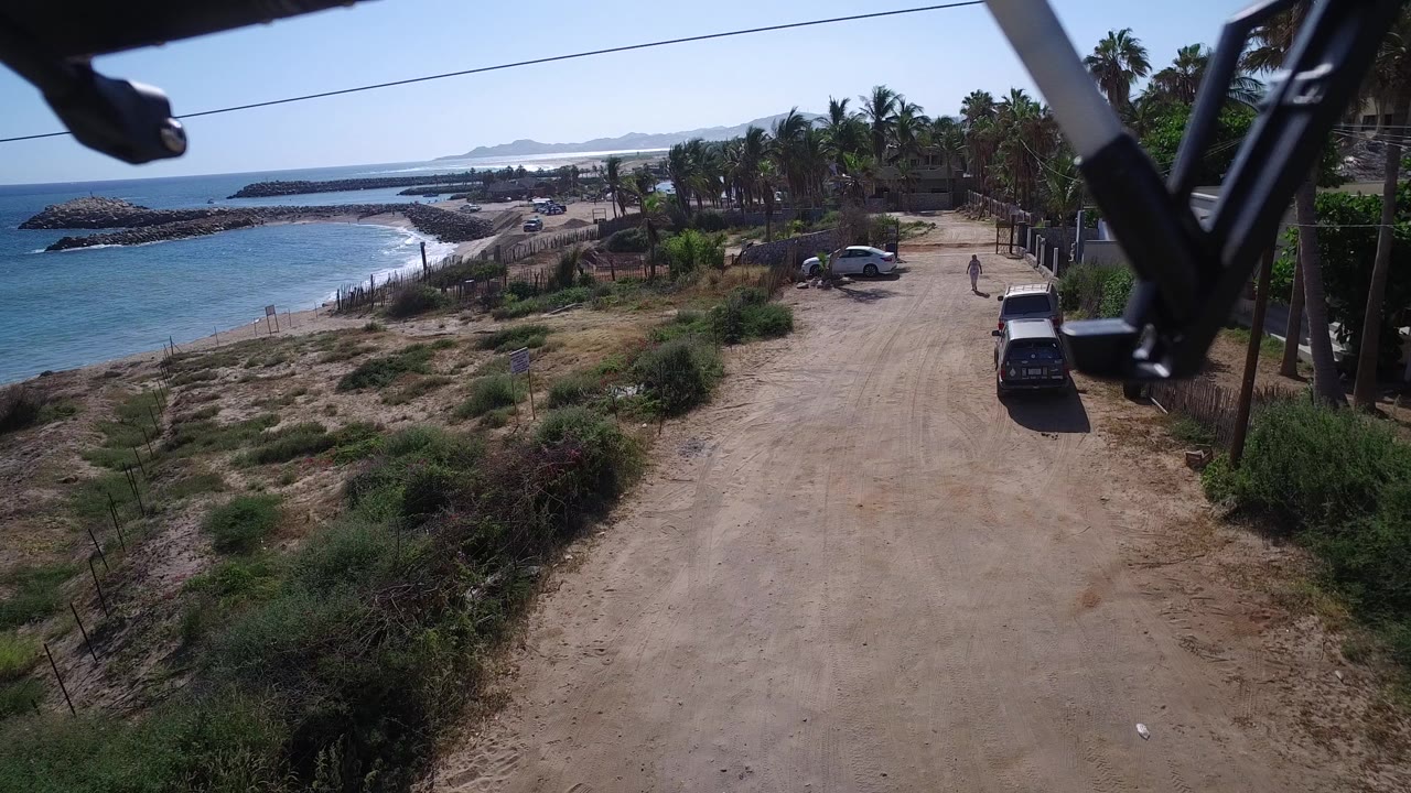 Low drone view over a dirt road beside blue ocean and scrub.