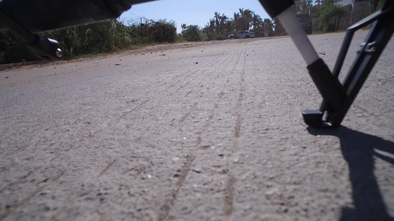 Low pavement view with a metal vehicle leg and roadside trees.