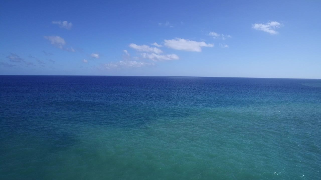 Blue ocean horizon under a pale sky with small clouds