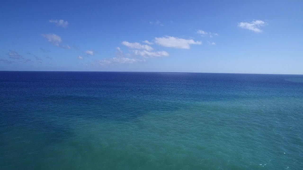 Open sea off Playita with a level horizon, darker offshore water, lighter turquoise foreground water, thin cloud patches, and no visible people.