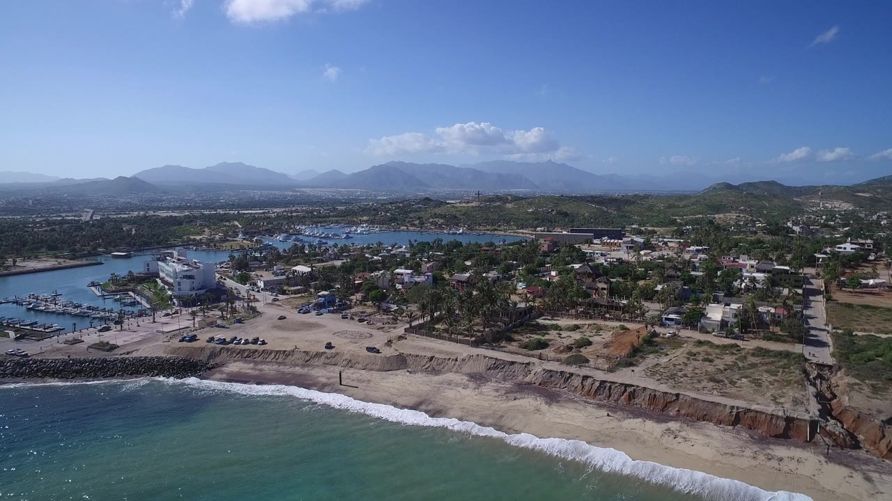 Aerial view of ocean, sandy bluff, coastal homes, marina docks, and distant mountains.