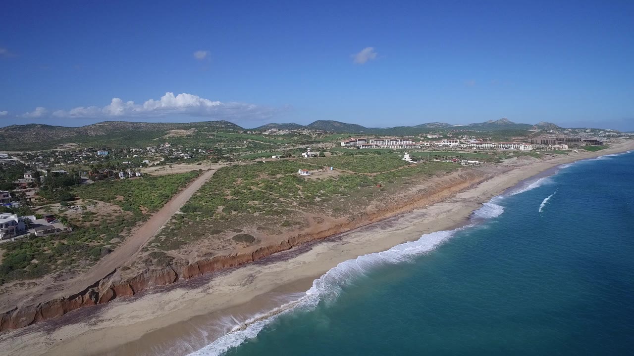Aerial view of blue ocean waves reaching a sandy beach below coastal bluffs.