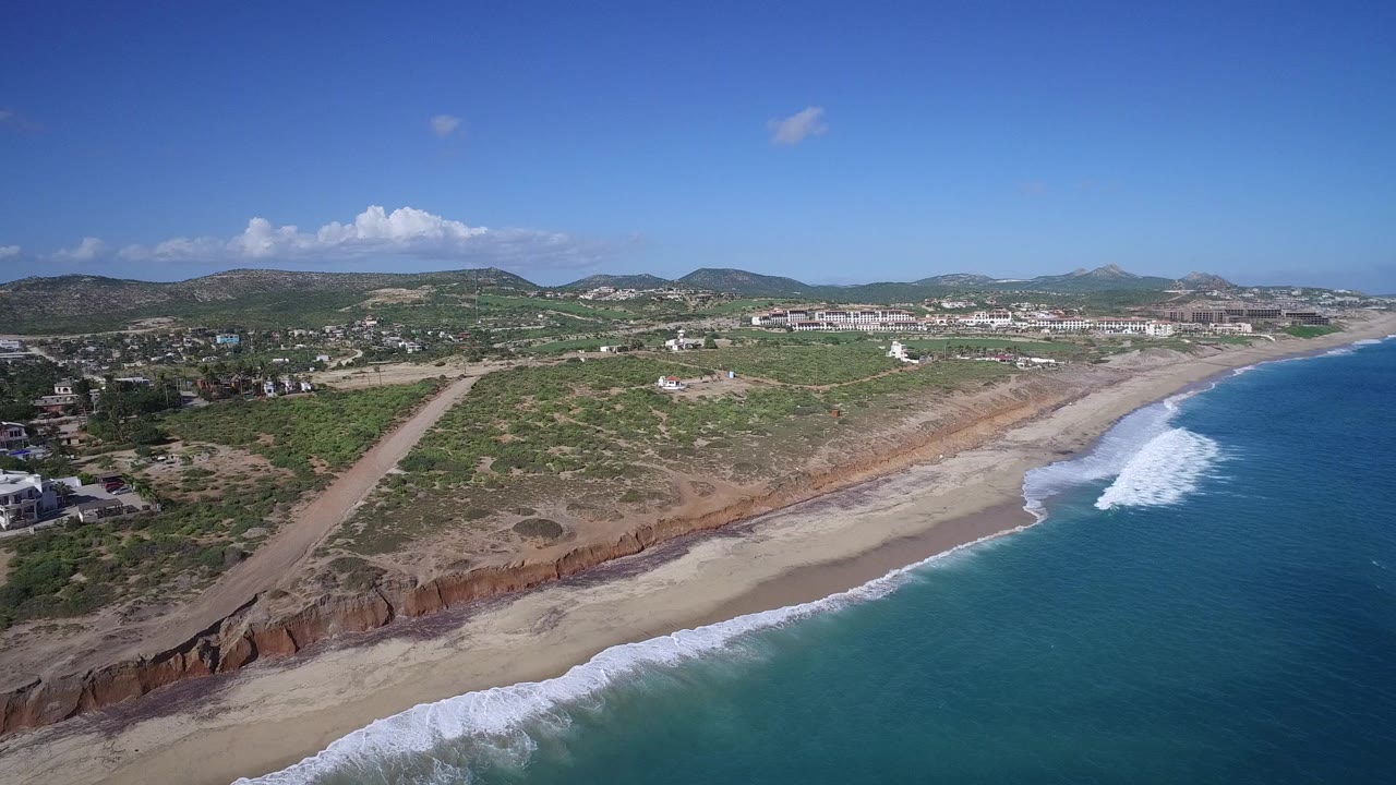 Aerial view of beach, ocean, bluffs, low vegetation, houses, and distant hills.