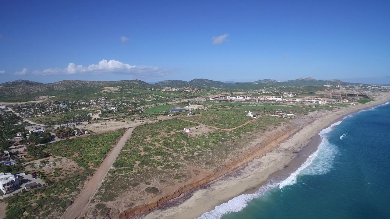 Drone view of shoreline with surf, open land, roads, and distant town.