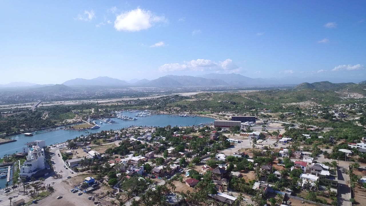 Aerial view of a coastal town, marina water, hills, and blue sky.
