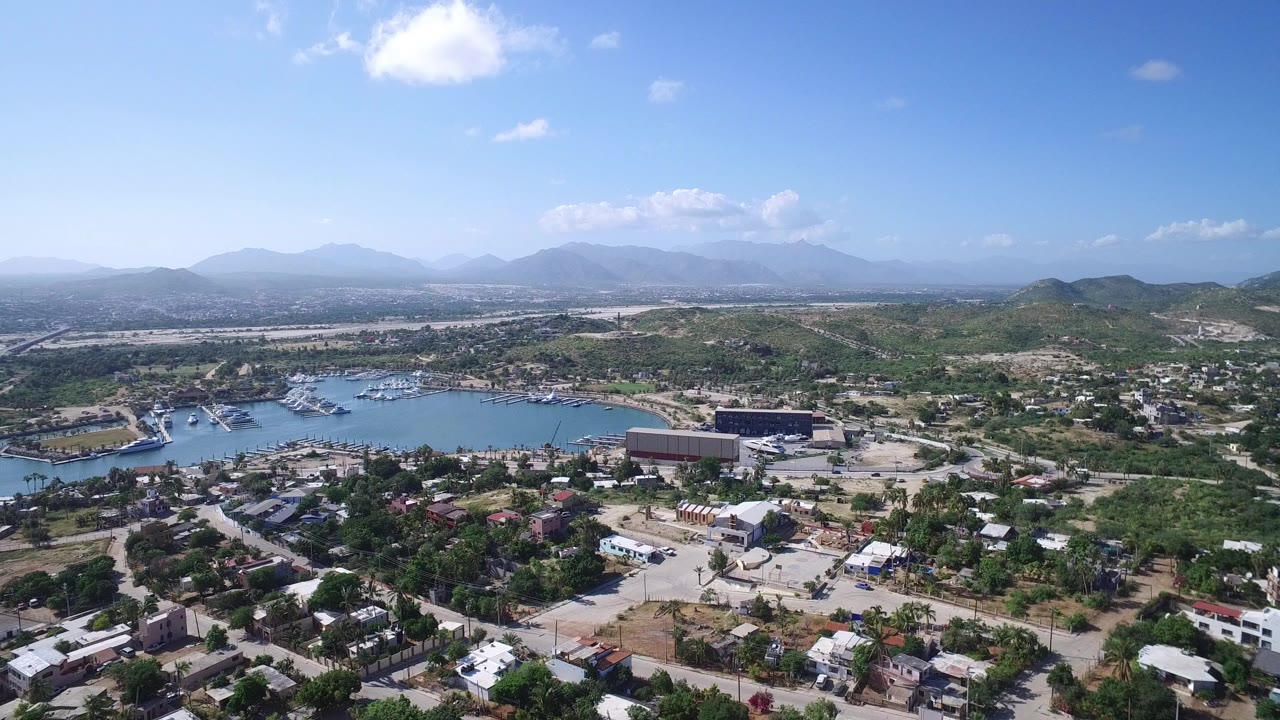 Aerial view of marina, town, hills, and distant mountains under a blue sky.