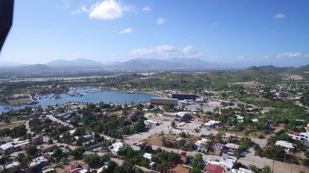 Wide aerial view over houses, streets, water, hills, and distant mountains.