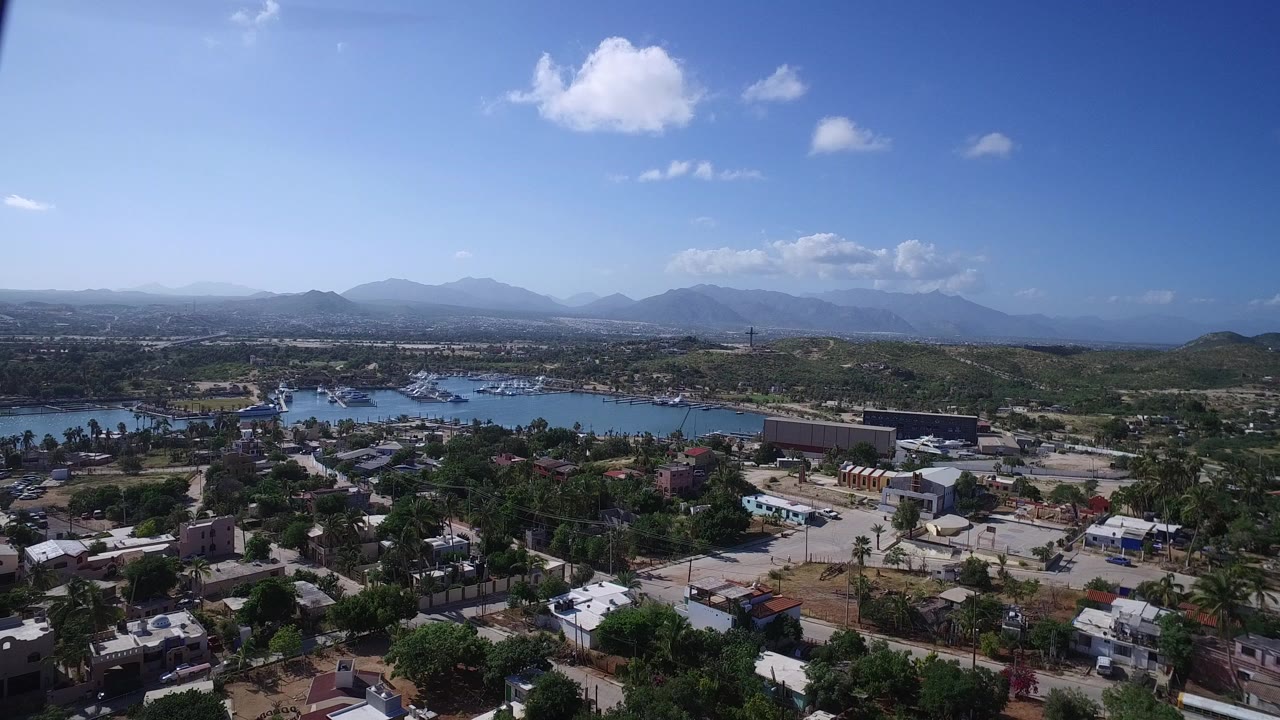Aerial view of village rooftops, water, and distant mountains under blue sky.